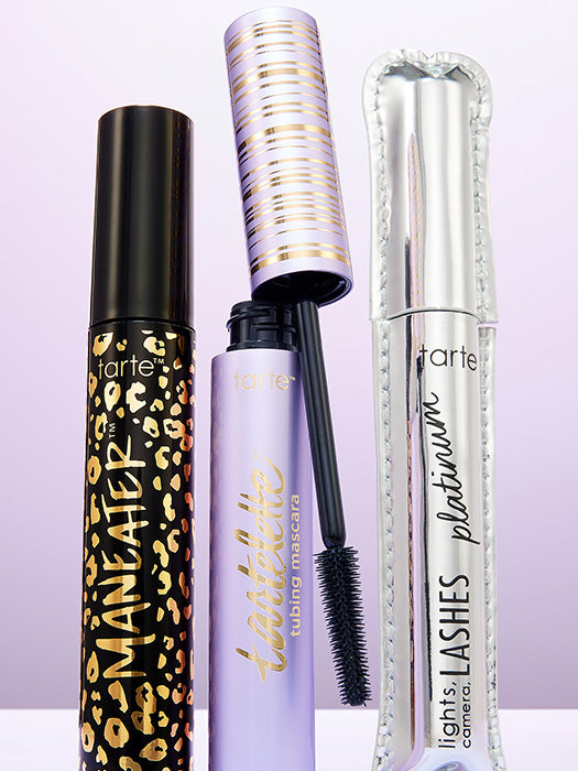 Three Tarte Cosmetics mascara tubes stand upright. The left tube features a leopard pattern, the center tube is purple with an open black brush, and the right tube is silver.
