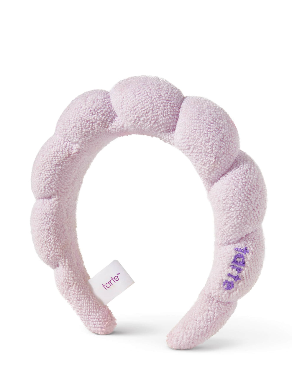 A plush, lilac headband arches in a standalone position. tarte is embroidered on the side, and a small tag with tarte dangles beneath, set against a plain white background.