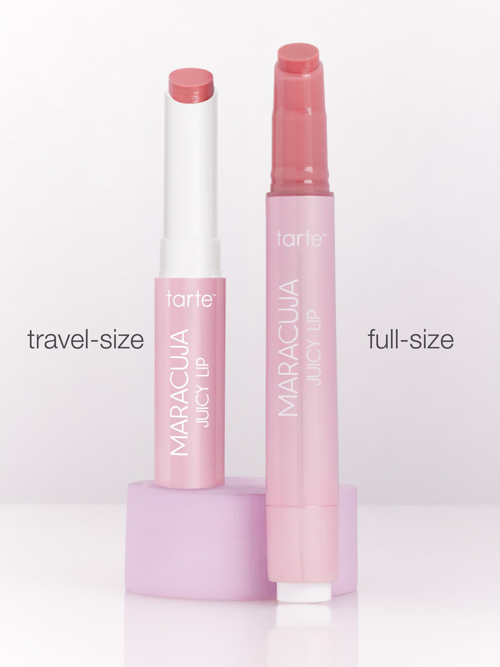 Two Tarte Cosmetics Maracuja Juicy Lip products, labeled travel-size and full-size, stand upright on a light purple platform against a plain background.
