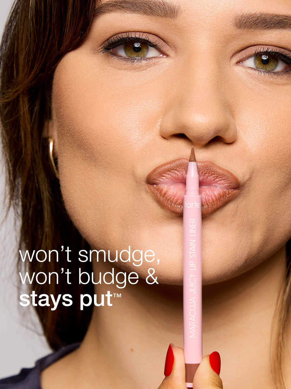 Woman holding a pink lip liner with text 'won't smudge, won't budge & stays put' on a gray background