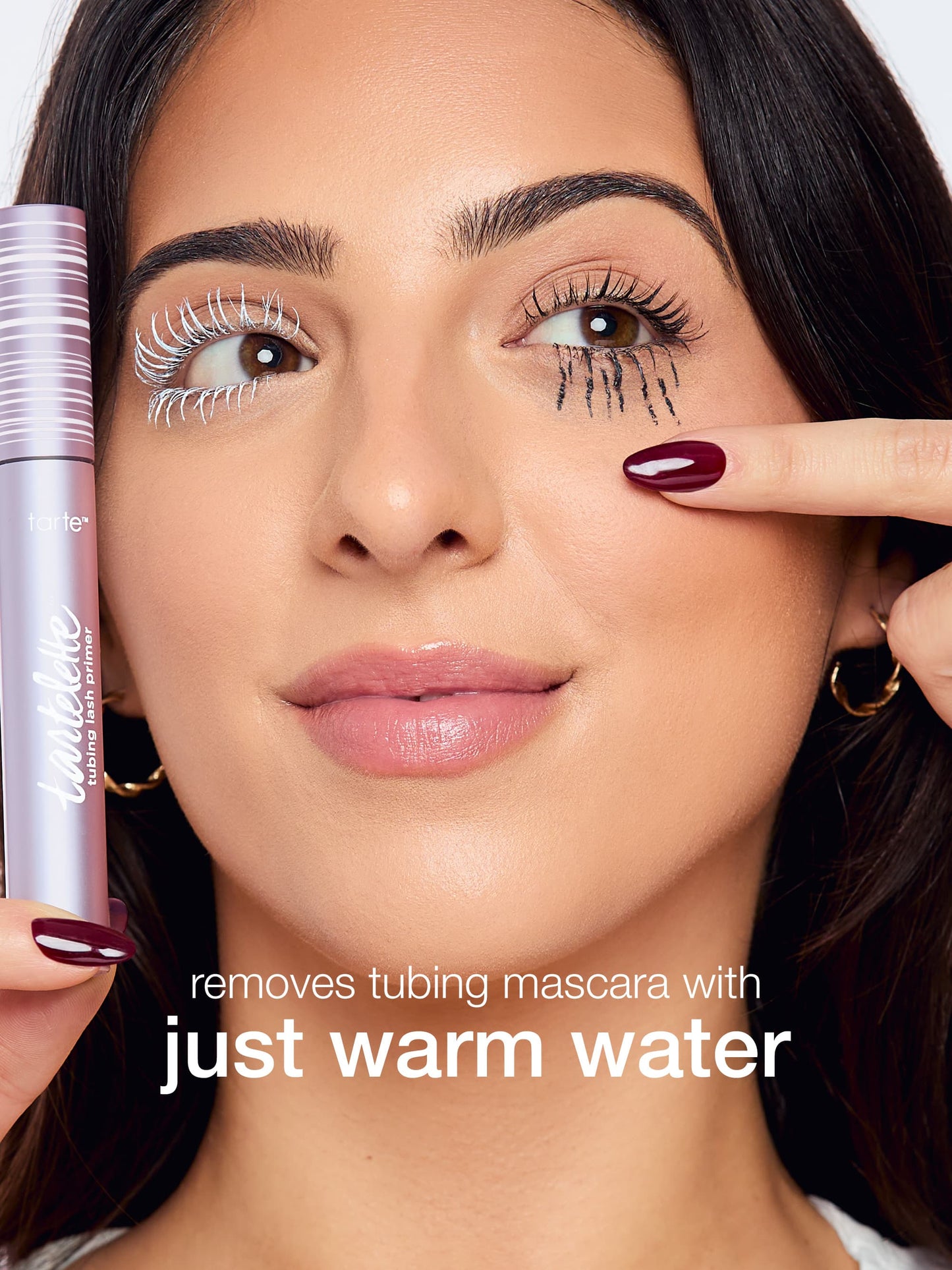 Woman applying mascara with a product labeled 'removes tubing mascara with just warm water'.