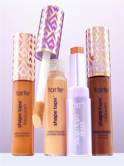Four Tarte Cosmetics concealers are displayed, standing upright against a gradient background. One has its applicator wand partially removed. Text: shape tape™ RADIANT, contour concealer, shape tape™ BLUR, shape tape™ CREAMY, ultra creamy.