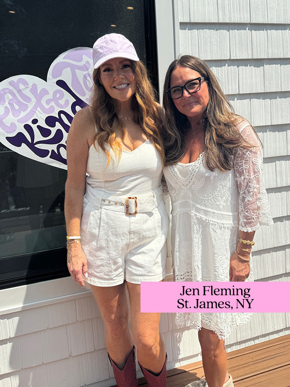 Two women stand side by side, smiling, in front of a window with a heart-shaped sign reading take time to be kind. Nearby text reads Jen Fleming, St. James, NY.