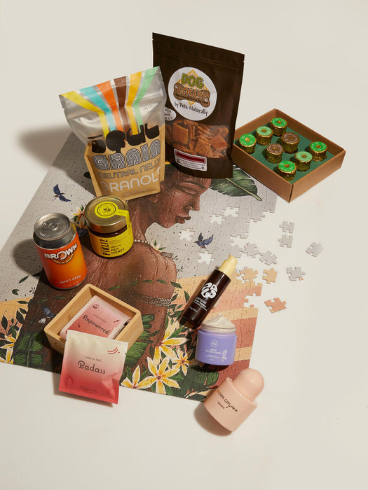 A variety of products, including granola, dog treats, beverages, skincare items, and confectionery, are arranged on a partially completed jigsaw puzzle depicting a woman with flowers, highlighting diverse lifestyles.