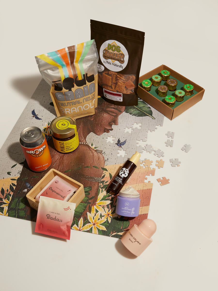 A variety of products, including granola, dog treats, beverages, skincare items, and confectionery, are arranged on a partially completed jigsaw puzzle depicting a woman with flowers, highlighting diverse lifestyles.