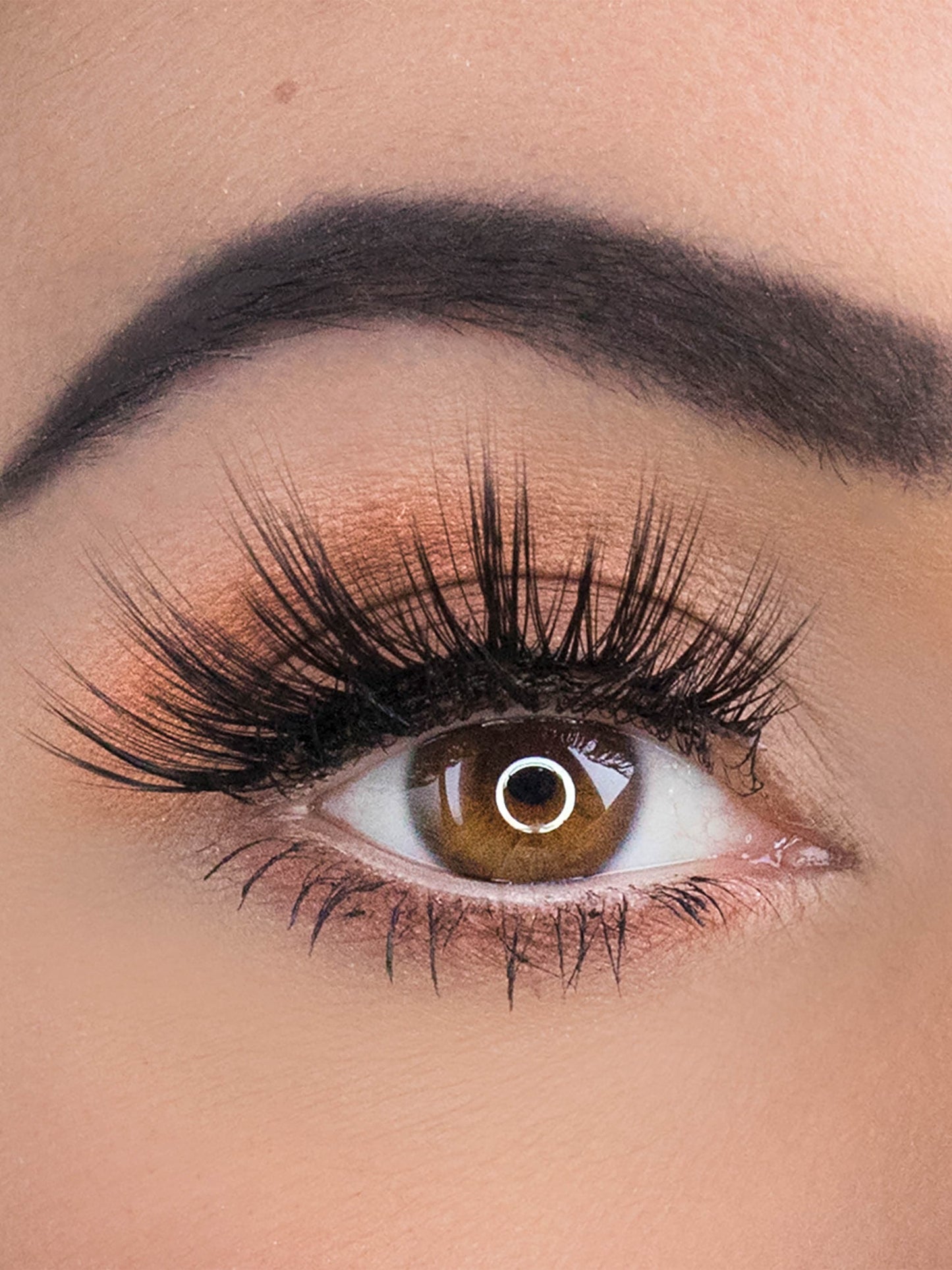 Close-up of an eye with long, dark eyelashes and a neutral background