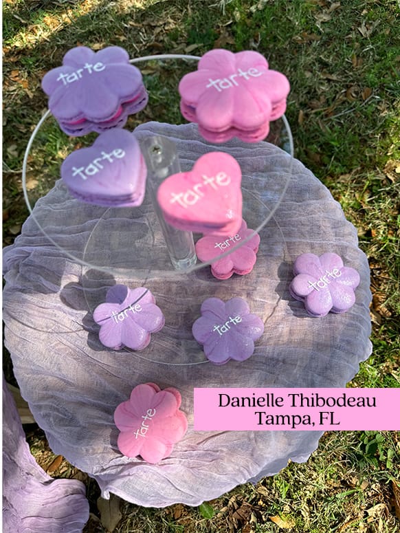 Colorful, flower-shaped macarons with tarte text displayed on a tiered stand; set outdoors on a draped cloth table. Text: Danielle Thibodeau, Tampa, FL.